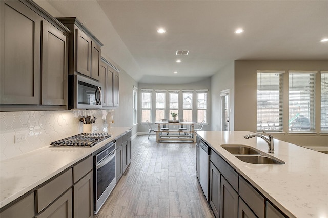 kitchen with sink, stainless steel appliances, light stone countertops, decorative backsplash, and light wood-type flooring