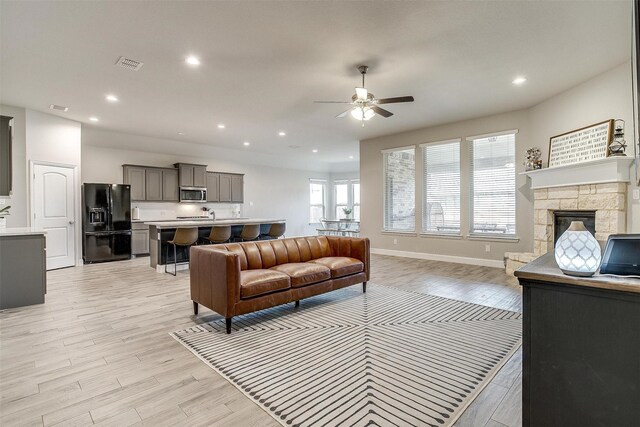 living room with a stone fireplace, light hardwood / wood-style floors, and ceiling fan