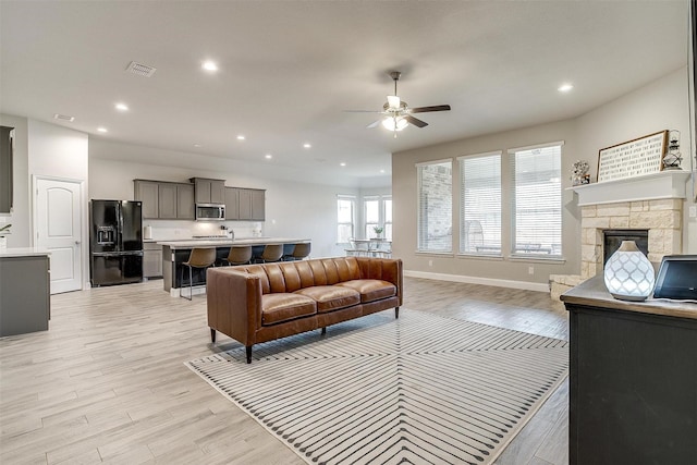 living room featuring ceiling fan, light hardwood / wood-style flooring, and a fireplace