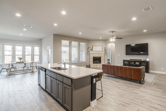 kitchen featuring a fireplace, sink, stainless steel dishwasher, light hardwood / wood-style floors, and a center island with sink