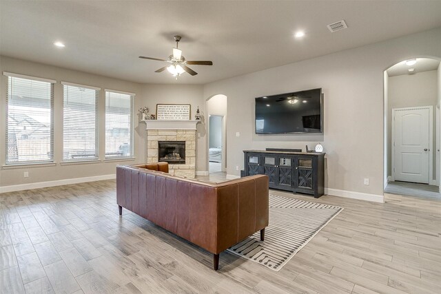 living room featuring ceiling fan, light hardwood / wood-style flooring, and a stone fireplace