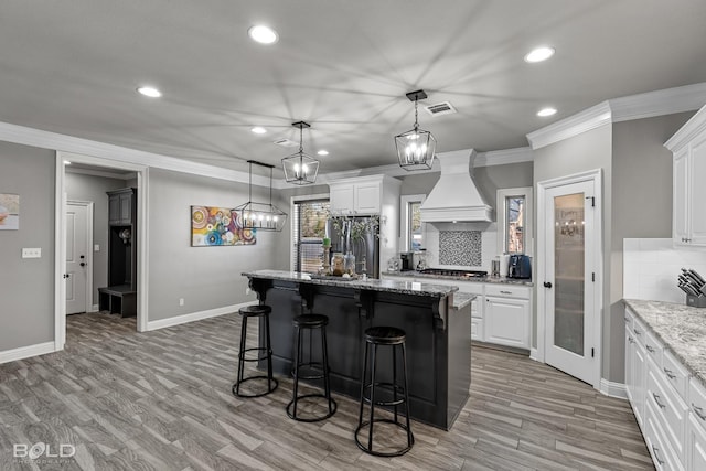 kitchen with a kitchen island with sink, backsplash, custom range hood, and white cabinetry