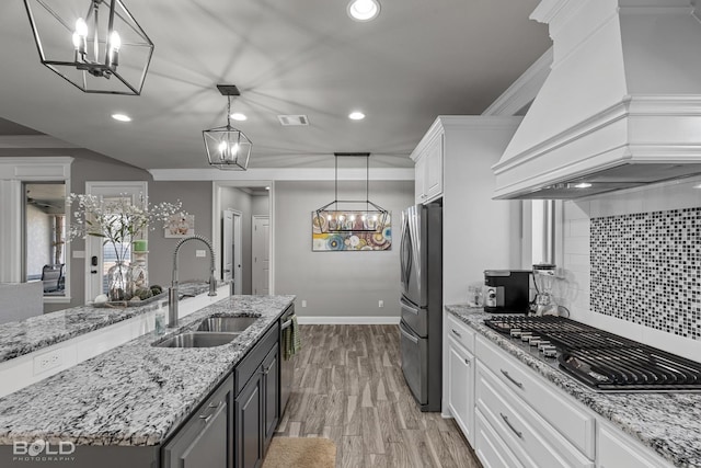 kitchen featuring hanging light fixtures, stainless steel appliances, custom range hood, white cabinetry, and sink