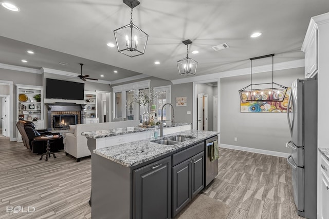 kitchen with a center island with sink, appliances with stainless steel finishes, pendant lighting, a brick fireplace, and white cabinets