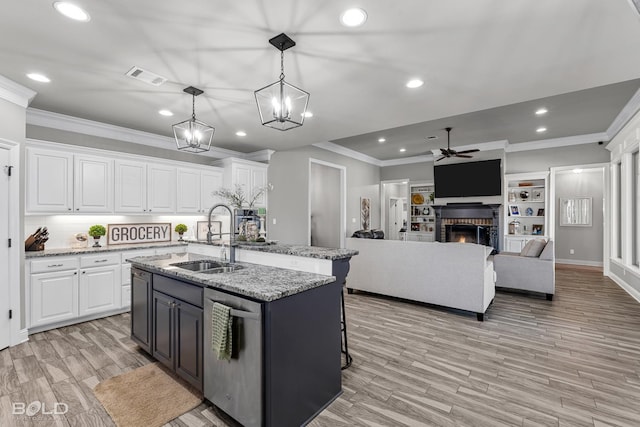 kitchen with sink, a center island with sink, white cabinets, and decorative light fixtures