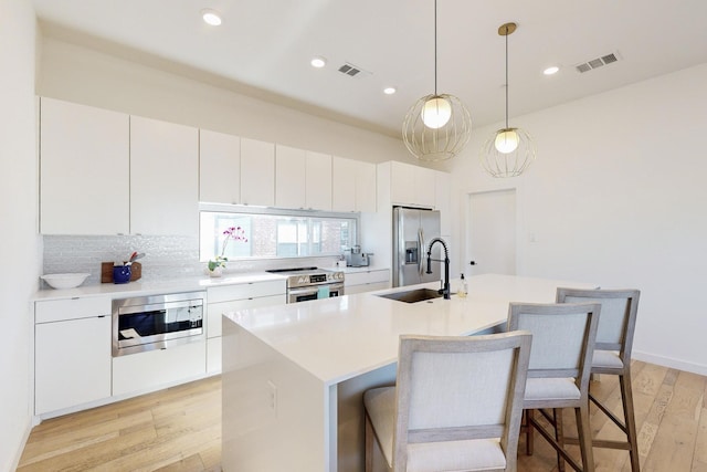 kitchen with sink, white cabinetry, an island with sink, hanging light fixtures, and appliances with stainless steel finishes