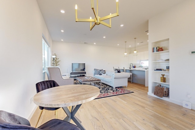 living room with sink, a chandelier, built in shelves, and light hardwood / wood-style flooring