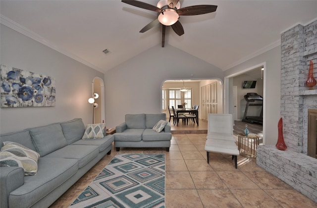 tiled living room featuring ornamental molding, ceiling fan, a brick fireplace, and vaulted ceiling with beams