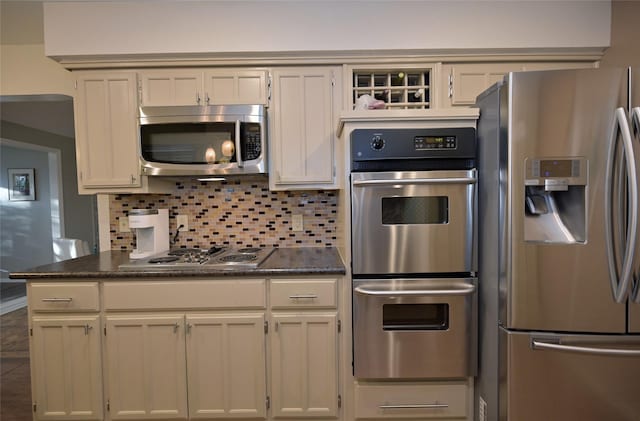 kitchen featuring stainless steel appliances, dark stone counters, white cabinetry, and decorative backsplash