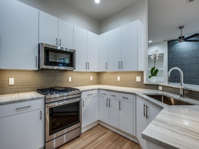 kitchen with appliances with stainless steel finishes, light hardwood / wood-style floors, ceiling fan, white cabinets, and sink