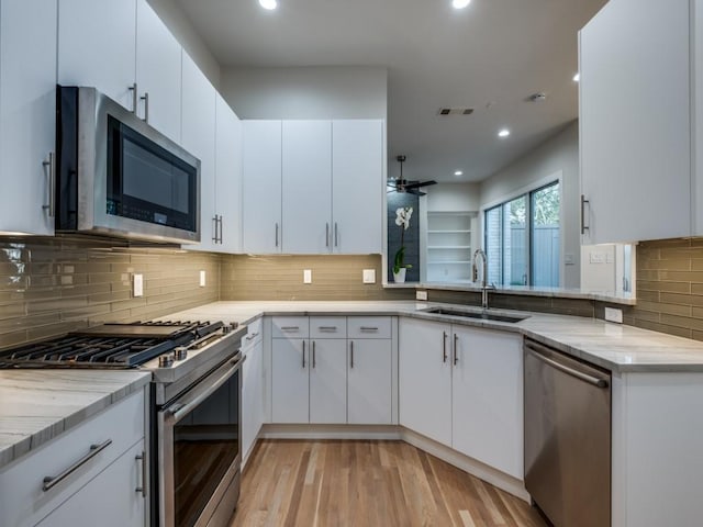 kitchen featuring sink, white cabinets, light wood-type flooring, kitchen peninsula, and appliances with stainless steel finishes