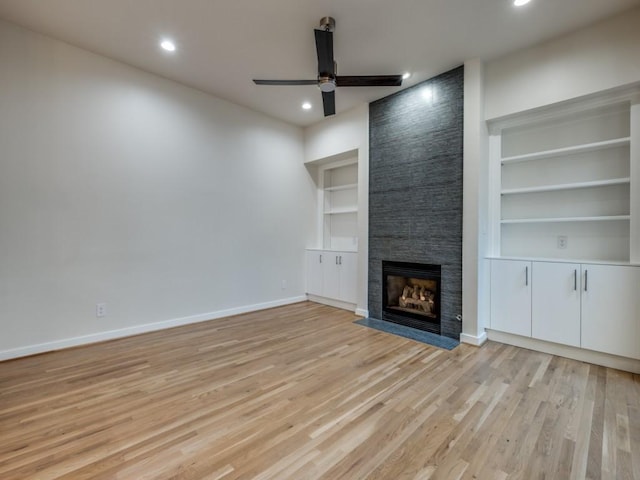 unfurnished living room with built in features, light wood-type flooring, a tiled fireplace, and ceiling fan