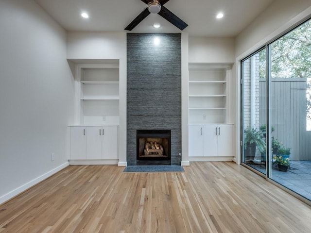 unfurnished living room with ceiling fan, light wood-type flooring, a fireplace, and built in shelves