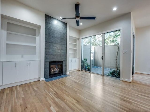 unfurnished living room featuring ceiling fan, light hardwood / wood-style flooring, built in shelves, and a fireplace