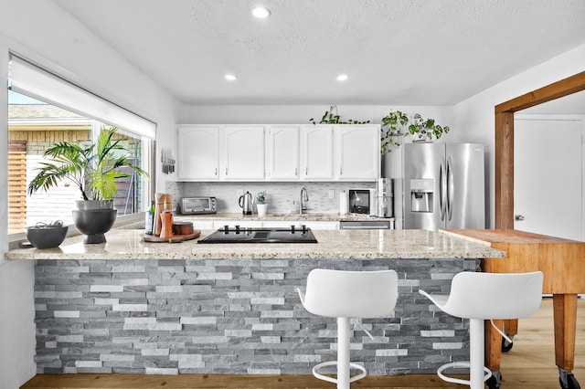 kitchen with light stone countertops, stainless steel fridge, a breakfast bar, black electric stovetop, and white cabinetry