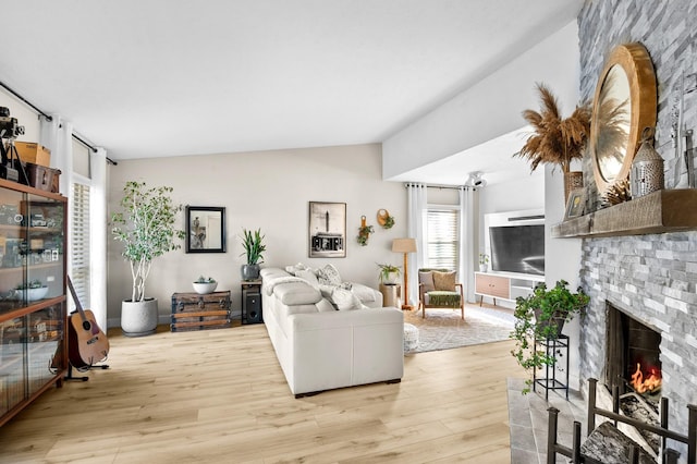 living room with light hardwood / wood-style flooring, a stone fireplace, and vaulted ceiling