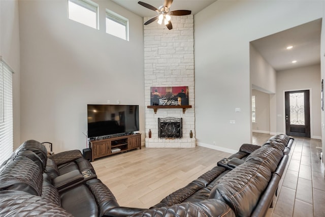 living room with a towering ceiling, a fireplace, ceiling fan, and light hardwood / wood-style flooring