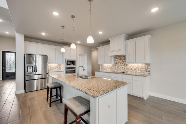 kitchen featuring hanging light fixtures, an island with sink, white cabinetry, appliances with stainless steel finishes, and sink