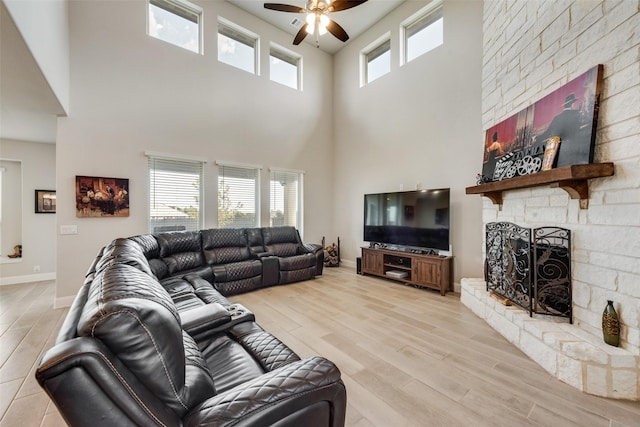 living room featuring a high ceiling, ceiling fan, light hardwood / wood-style flooring, and a stone fireplace