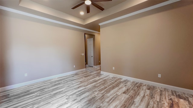 unfurnished room featuring a raised ceiling, crown molding, light wood-type flooring, and ceiling fan