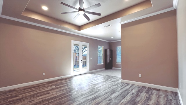 empty room featuring wood-type flooring, ceiling fan, a raised ceiling, crown molding, and french doors