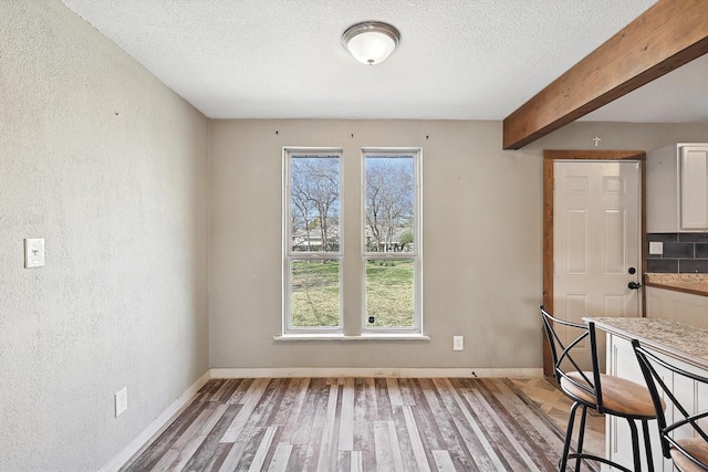 unfurnished dining area featuring a textured ceiling, beam ceiling, and hardwood / wood-style floors