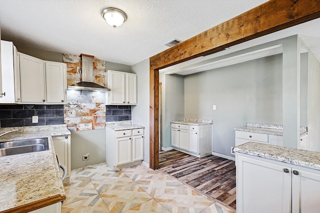 kitchen with sink, a textured ceiling, white cabinetry, wall chimney exhaust hood, and tasteful backsplash