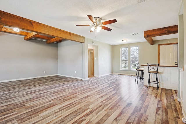 unfurnished living room featuring a textured ceiling, ceiling fan, light hardwood / wood-style flooring, and beamed ceiling