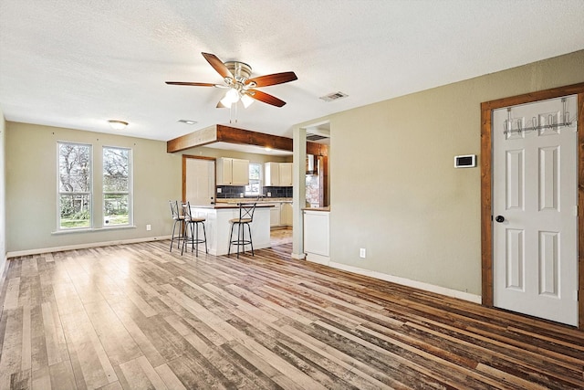 unfurnished living room featuring ceiling fan, light wood-type flooring, and a textured ceiling