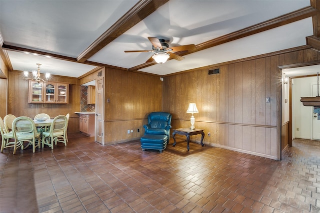 living area featuring ceiling fan with notable chandelier, ornamental molding, beamed ceiling, and wood walls