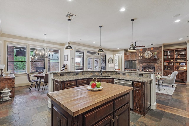 kitchen with decorative light fixtures, a large island with sink, a fireplace, and dark brown cabinets