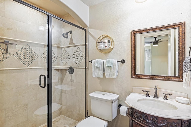 bathroom with toilet, ceiling fan, a shower with shower door, and vanity