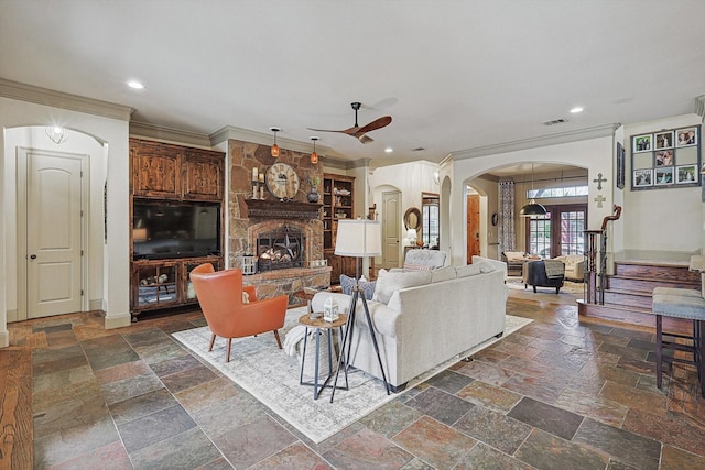 living room with ceiling fan, crown molding, and a stone fireplace