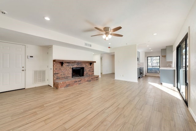 unfurnished living room featuring a fireplace, ceiling fan, light hardwood / wood-style floors, and sink