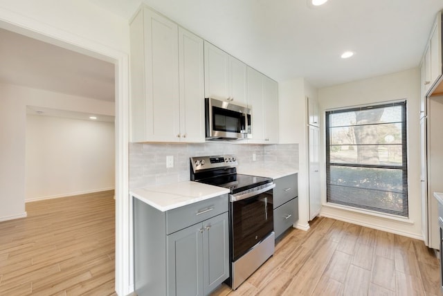 kitchen featuring gray cabinets, light hardwood / wood-style floors, stainless steel appliances, light stone counters, and white cabinetry