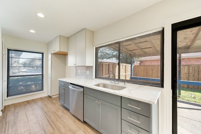 kitchen featuring gray cabinetry, light stone countertops, sink, stainless steel dishwasher, and tasteful backsplash