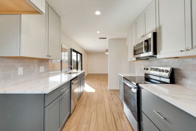 kitchen with stainless steel appliances, light stone counters, tasteful backsplash, light hardwood / wood-style floors, and gray cabinetry