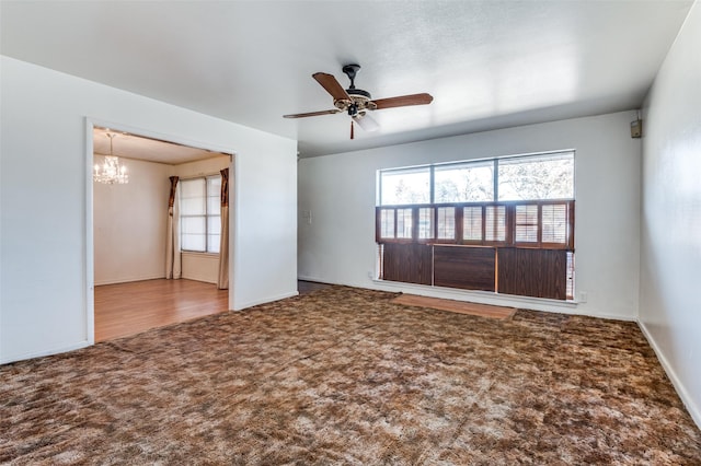 carpeted empty room featuring ceiling fan with notable chandelier