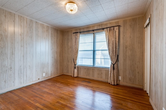 empty room with crown molding, wood walls, and hardwood / wood-style flooring