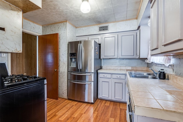 kitchen with gray cabinets, light hardwood / wood-style floors, stainless steel appliances, ornamental molding, and sink