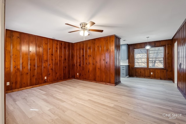 empty room featuring ceiling fan, light hardwood / wood-style flooring, and wooden walls