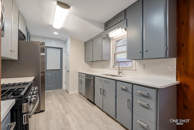 kitchen featuring light hardwood / wood-style floors, tasteful backsplash, gray cabinetry, appliances with stainless steel finishes, and sink