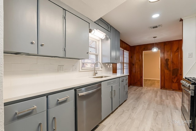 kitchen with appliances with stainless steel finishes, hanging light fixtures, light wood-type flooring, decorative backsplash, and sink