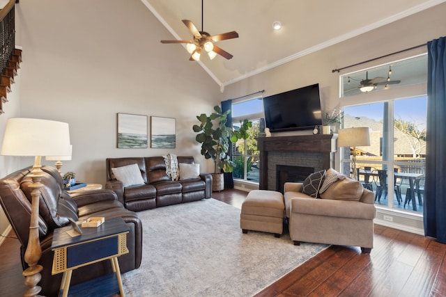 living room featuring ceiling fan, high vaulted ceiling, dark hardwood / wood-style flooring, crown molding, and a stone fireplace