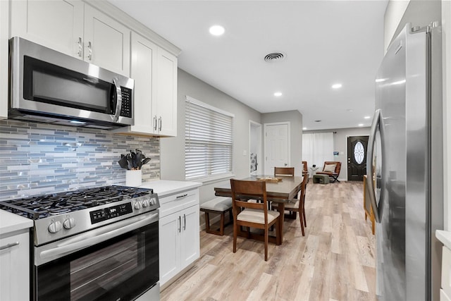 kitchen featuring light wood-type flooring, backsplash, stainless steel appliances, and white cabinetry