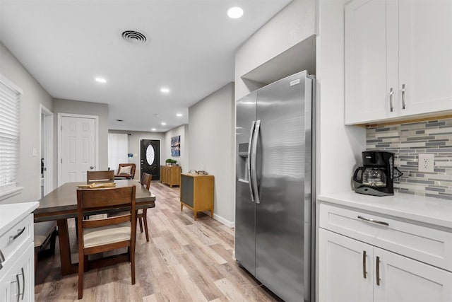 kitchen featuring stainless steel refrigerator with ice dispenser, decorative backsplash, white cabinets, and light wood-type flooring