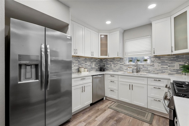 kitchen with white cabinetry, stainless steel appliances, tasteful backsplash, light wood-type flooring, and sink