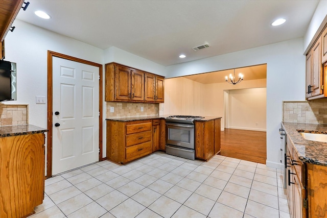 kitchen with an inviting chandelier, stainless steel range with gas cooktop, decorative backsplash, and light tile patterned floors