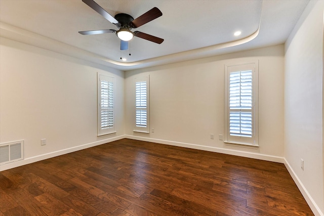 spare room featuring ceiling fan, a healthy amount of sunlight, a tray ceiling, and dark wood-type flooring