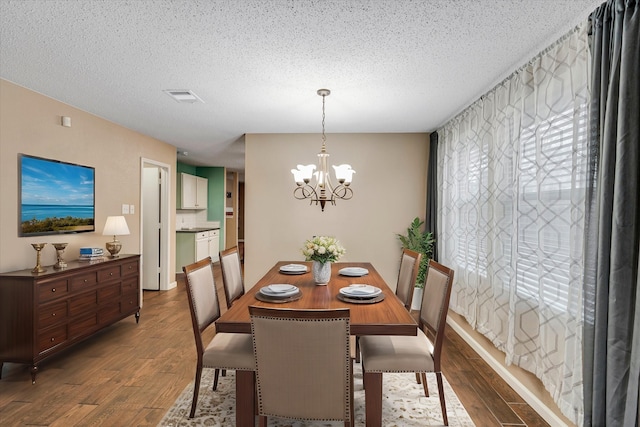 dining space featuring dark wood-type flooring, a textured ceiling, and an inviting chandelier